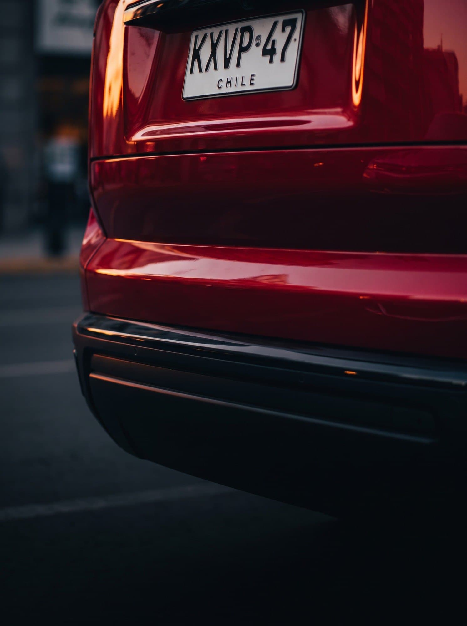 Parte trasera de un auto rojo con su patente chilena a la vista, al atardecer